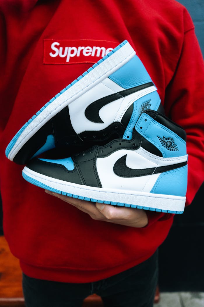 A person holds a stylish pair of Air Jordan sneakers against a red Supreme hoodie.