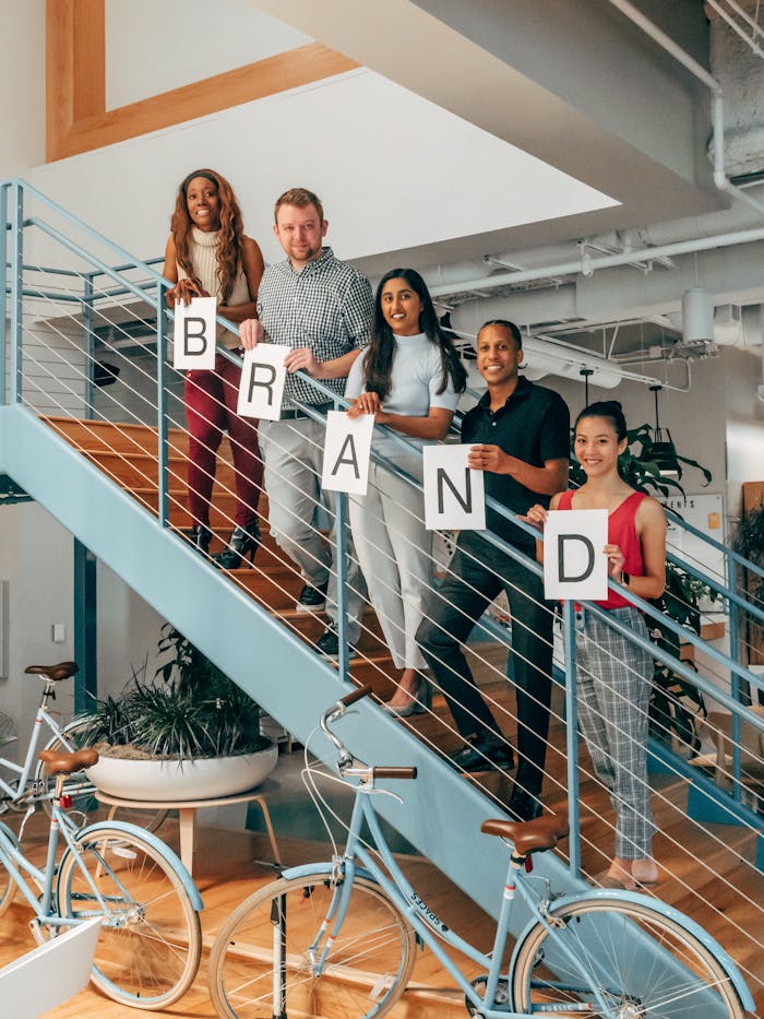 The Art of Drawing Readers In: Your attractive post title goes here A diverse group of colleagues smiling and holding a 'Brand' sign on indoor office stairs.